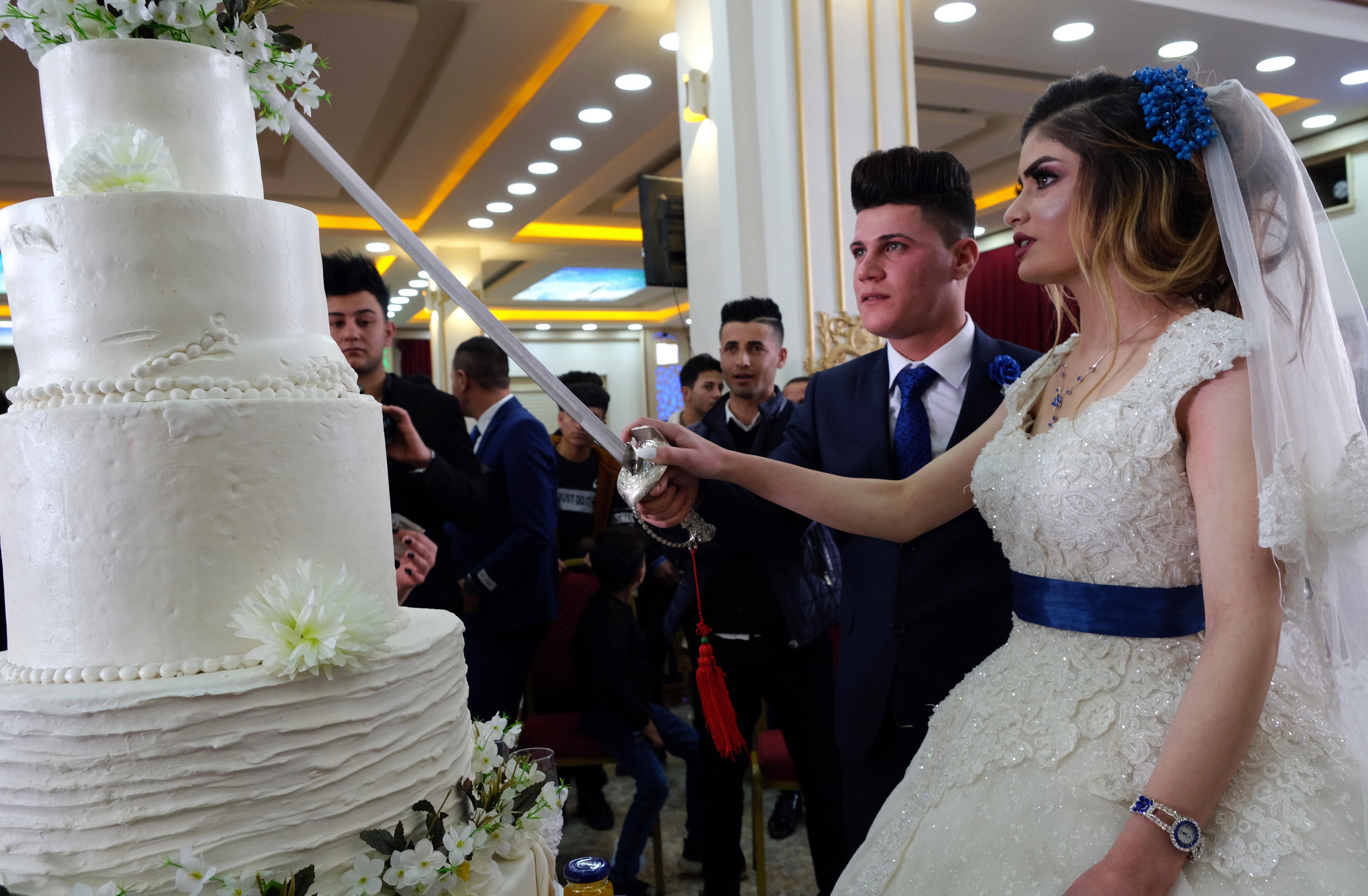 Sundus Garis (R), 16, and Farid Mallo, 19, both from the beleaguered Yazidi community who were displaced from northern Iraq's Sinjar region, cut the cate with a sword during their wedding ceremony in the northernwestern Iraqi Kurdish city of Dohuk, near the border with Turkey, on January 23, 2020. - Sinjar, a region west of the northern Iraqi city of Mosul that was overrun by the extremist Islamic State (IS) group five years ago, is the historic home of the Yazidi minority which under went a brutal campaign waged by IS jihadists who forced children to become soldiers and used thousands of women as sex slaves. Only a sliver of Sinjar's native population of 500,000 Yazidis has returned since their region was taken back by Iraqi forces from IS in 2017, with the rest saying persistent destruction, the lack of services and the tense security situation have kept them in camps. (Photo by SAFIN HAMED / AFP) (Photo by SAFIN HAMED/AFP via Getty Images)